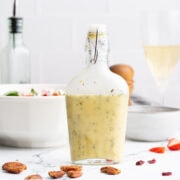Chardonnay vinaigrette in a jar on the table with salad and a glass of white wine.