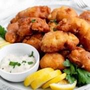 A plate of pancake batter fried fish with sauce on the side garnished with lemon slices.
