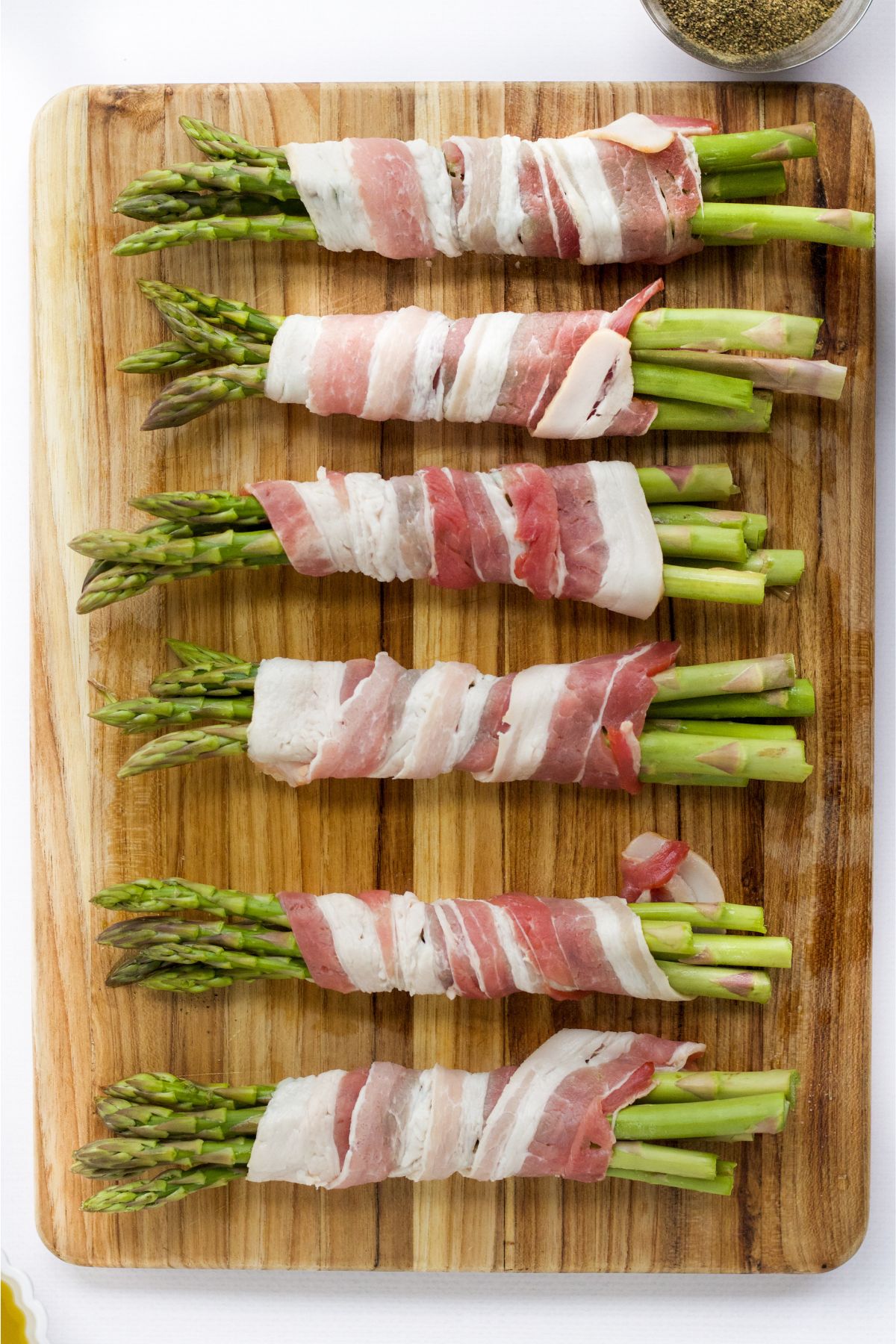 Bundles of asparagus with bacon wrapped around it on a cutting board.
