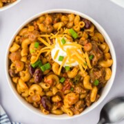 A bowl of Crockpot Cheesy Chili Mac with dollop of sour cream and some shredded cheddar.