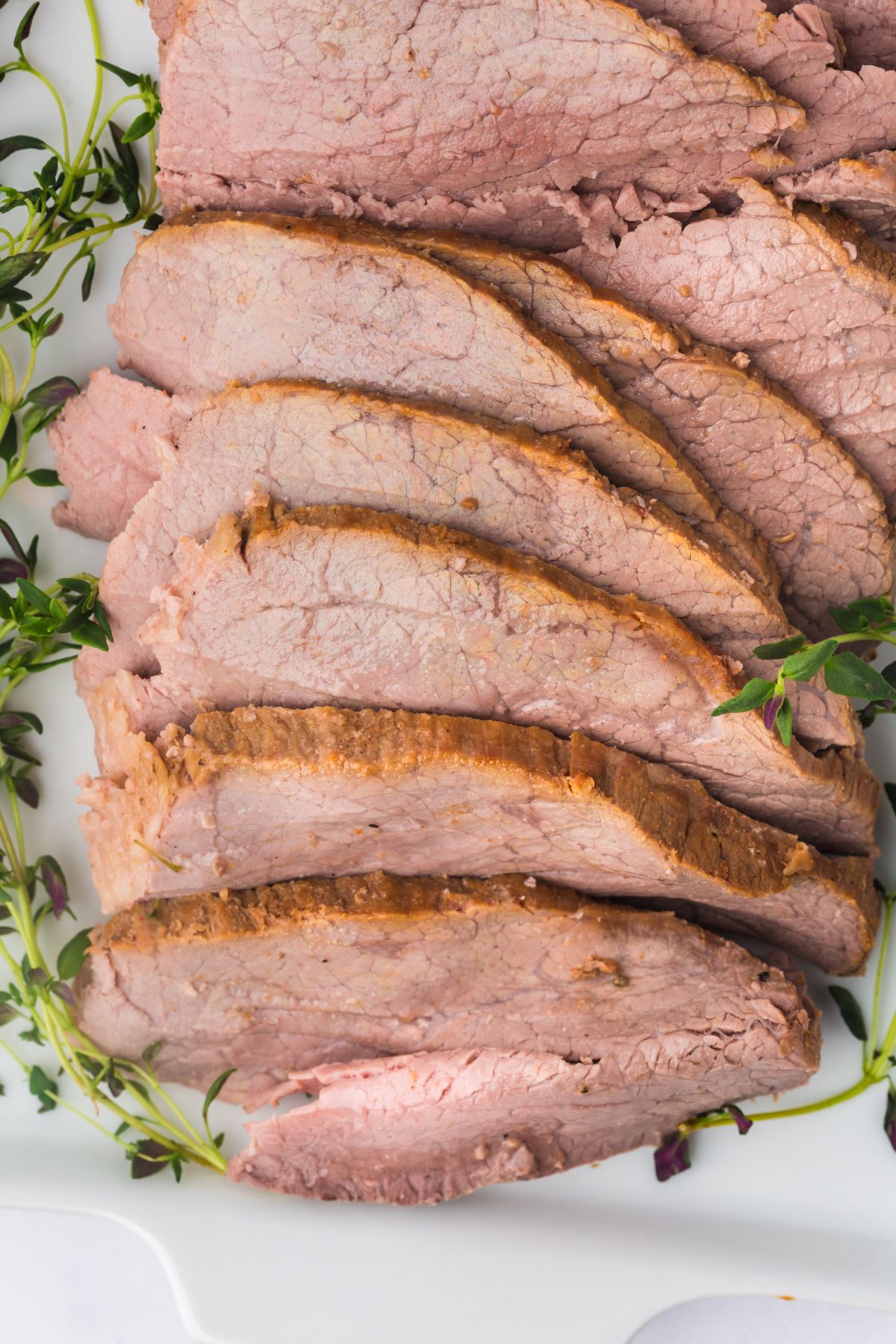 A plate full of sliced roast garnished with fresh herbs.