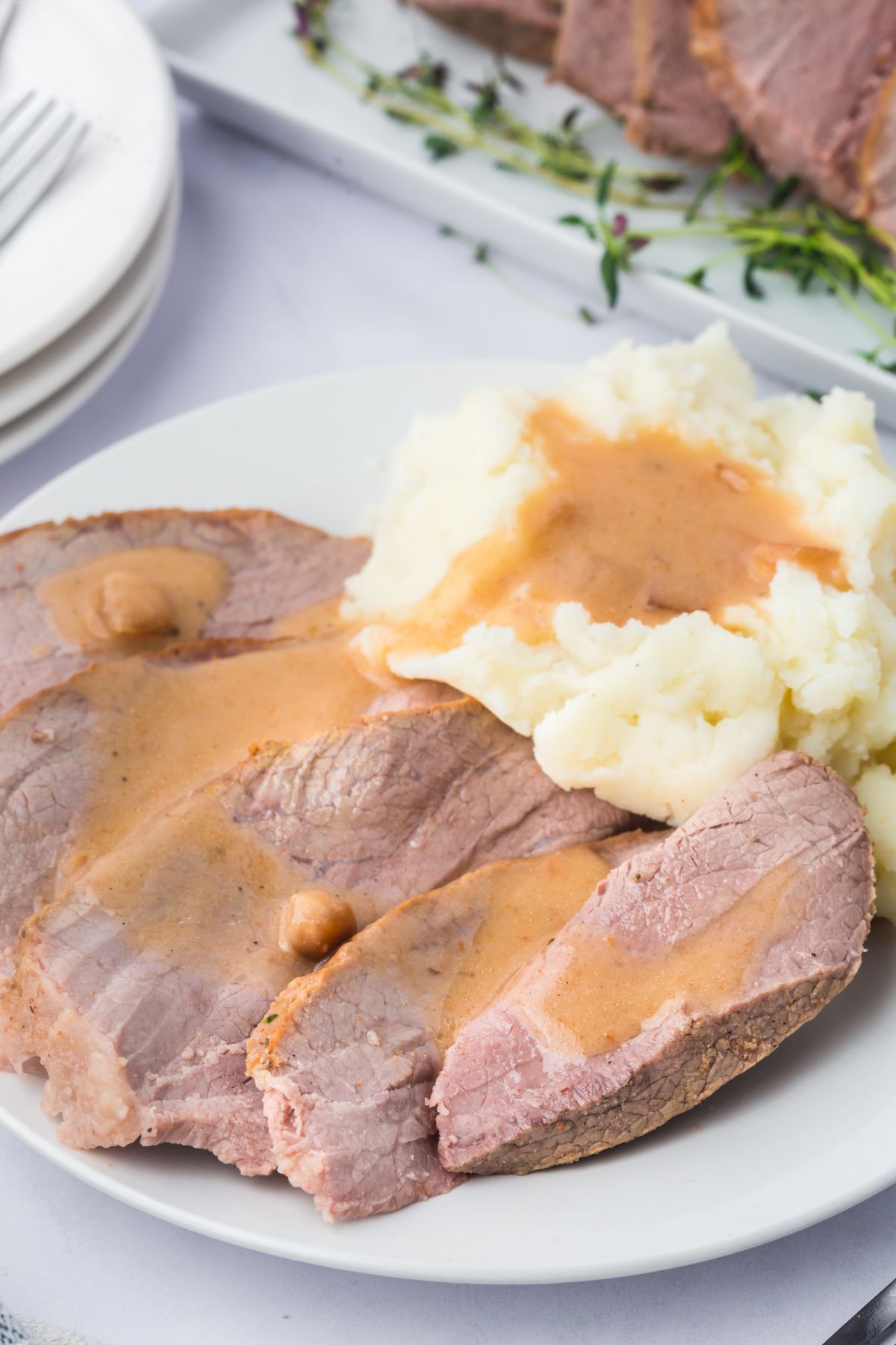Sliced eye of round roast with gravy with a side of mashed potatoes.
