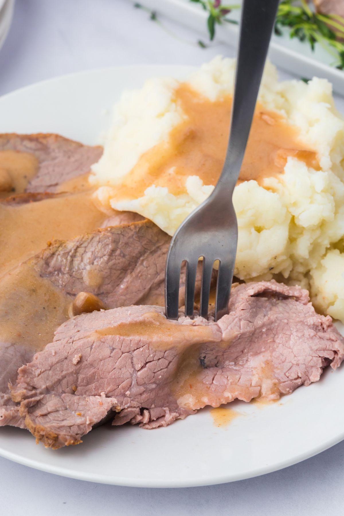 A fork picking up a slice of roast on a plate with a side of mashed potatoes.