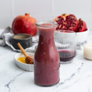Pomegranate vinaigrette dressing in glass bottle on the table in front a cut pomegranate and a glass of juice.