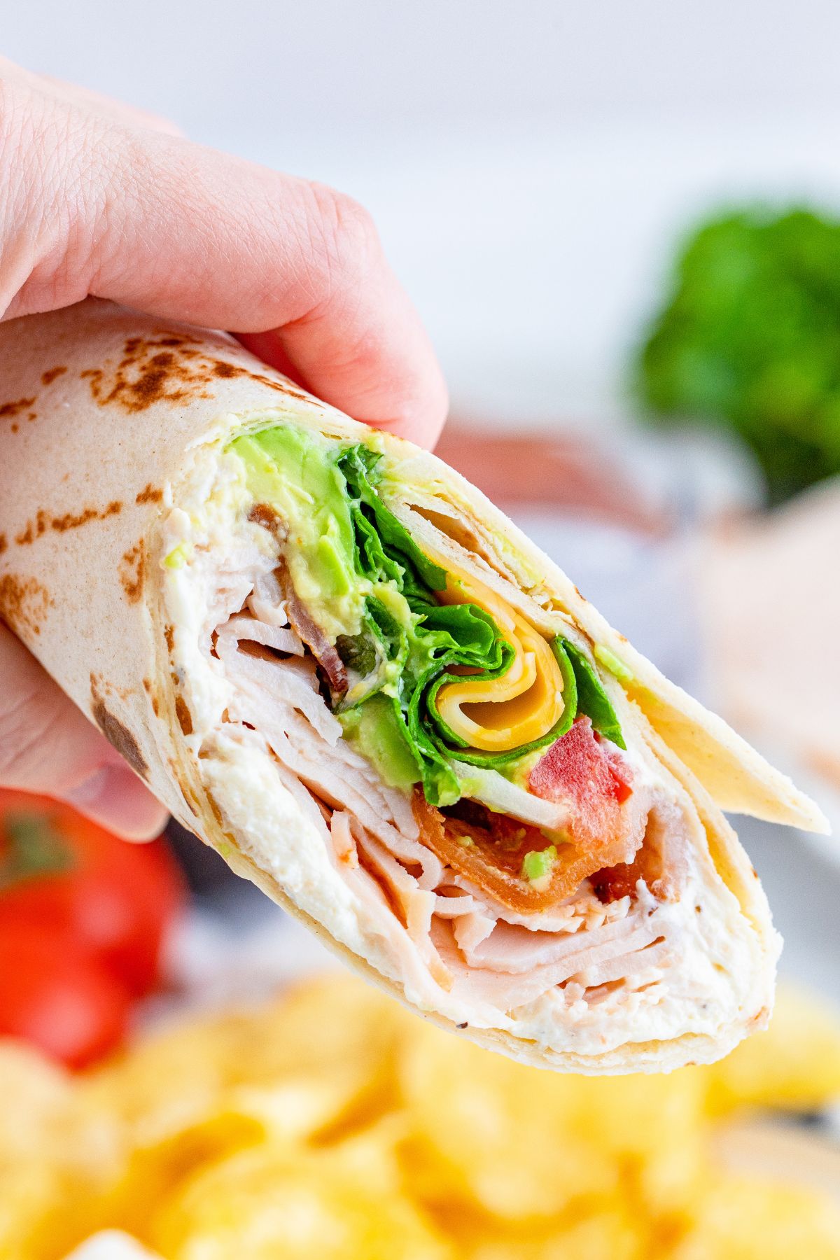 Turkey club wrap held up in the air by a hand.