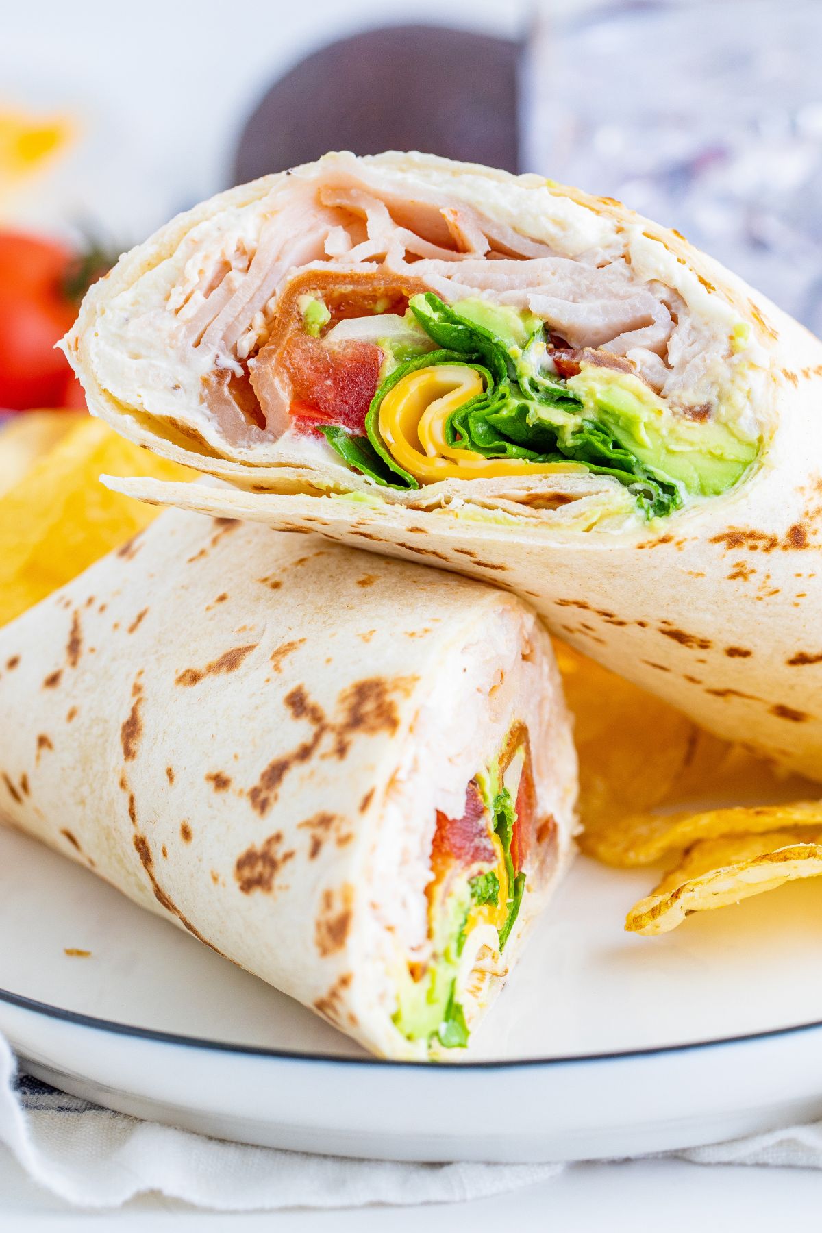 Turkey club wrap cut in half stacked on top of each other on a plate with some chips.