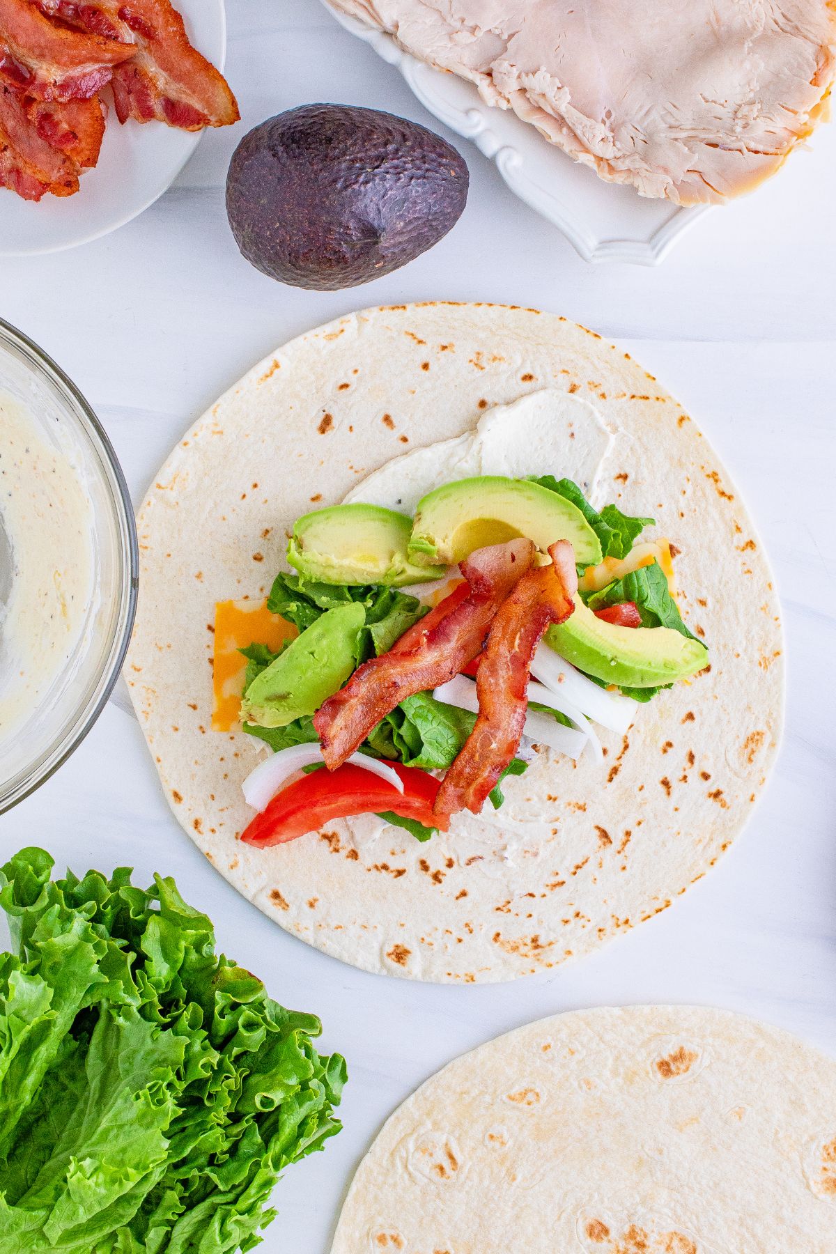 Cheese, bacon, onion, avocado, tomato, and lettuce on top of the tortilla.