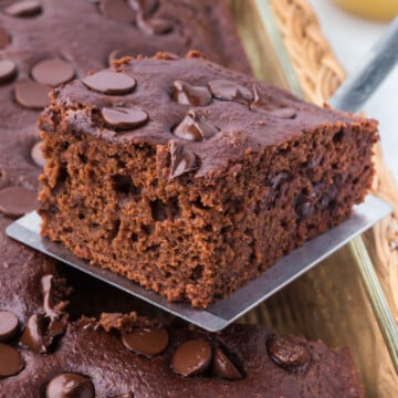 A slice of chocolate applesauce cake held in the air above the rest of the cake.