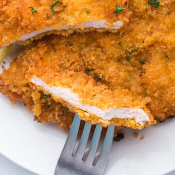 Pork schnitzel on a plate with a piece cut an don a fork.