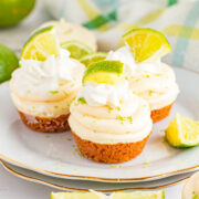 Three mini key lime pie bites on a plate with fresh lime pieces on top.