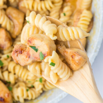 A wooden spoon full of honey mustard chicken pasta lifted out of the skillet.
