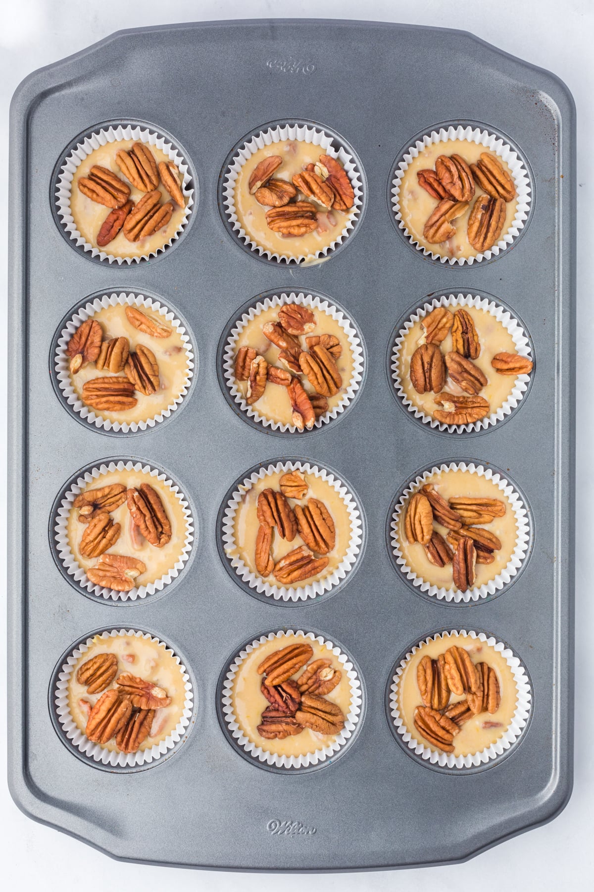 Pecan muffins topped with pecan halves before baking.