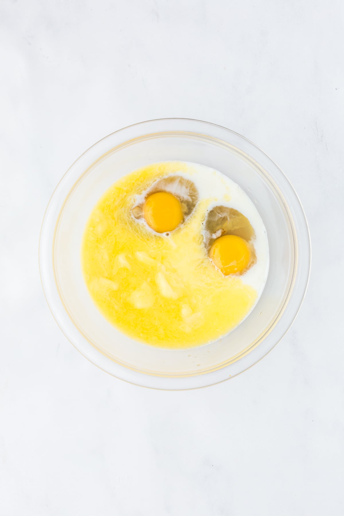 Butter, brown sugar, eggs, milk, vanilla, and maple syrup mixed together in a bowl.