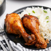 Closeup shot of Chinese honey chicken drumsticks with rice on plate.