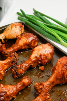 Chicken legs on a baking tray with green onions.