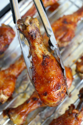 Tongs picking up a piece of honey chicken drumsticks to serve.