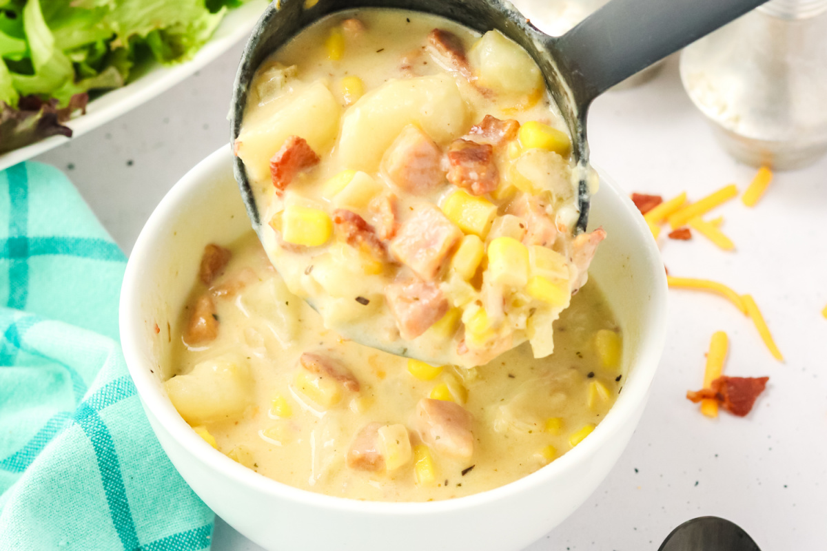 A bowl being filled with a spoon full of chowder.