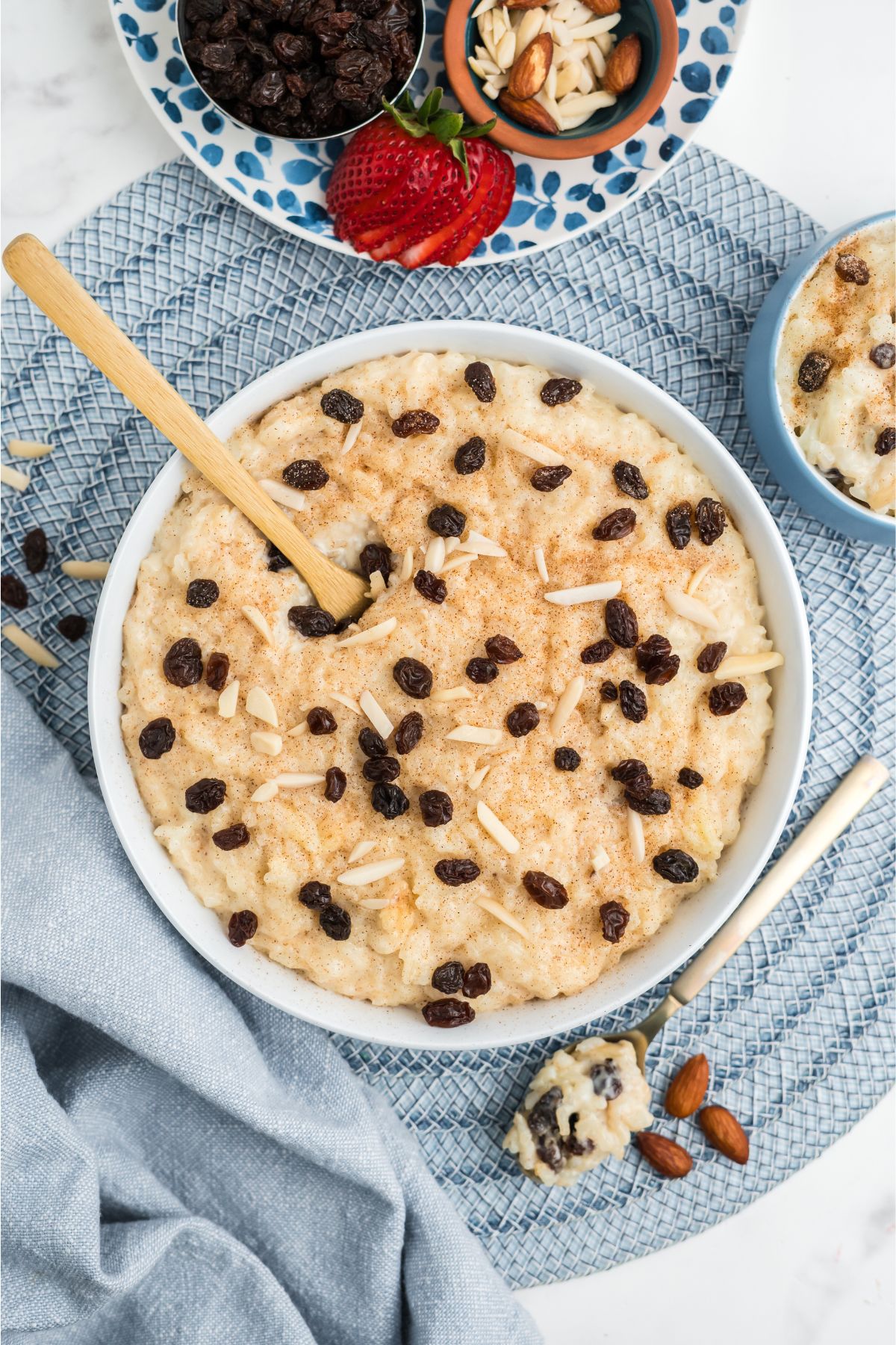 Rice pudding garnished with raisins and slivered almonds in a white bowl.