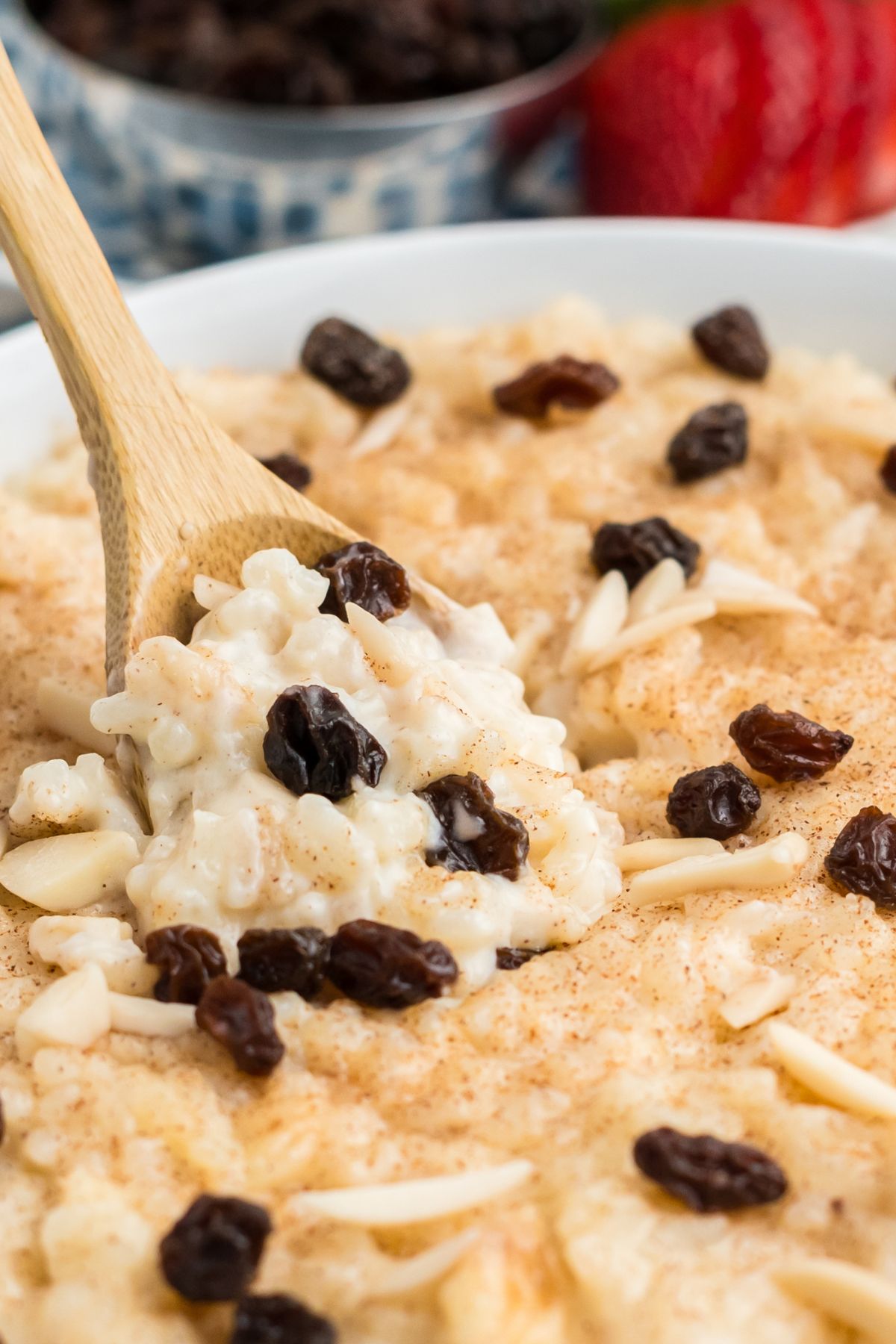 A wooden spoon scooping some rice pudding with raisins and almonds.