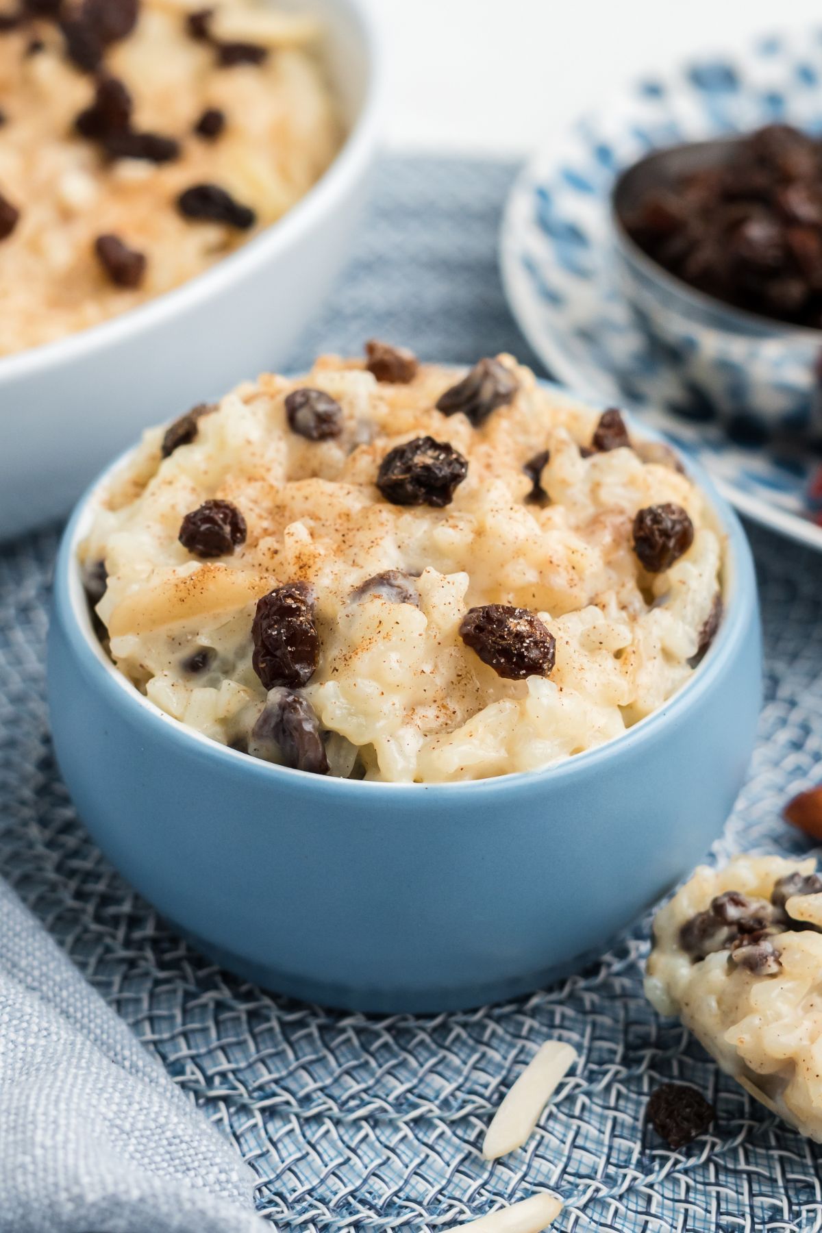 A blue bowl filled with rice pudding with raisins on top.