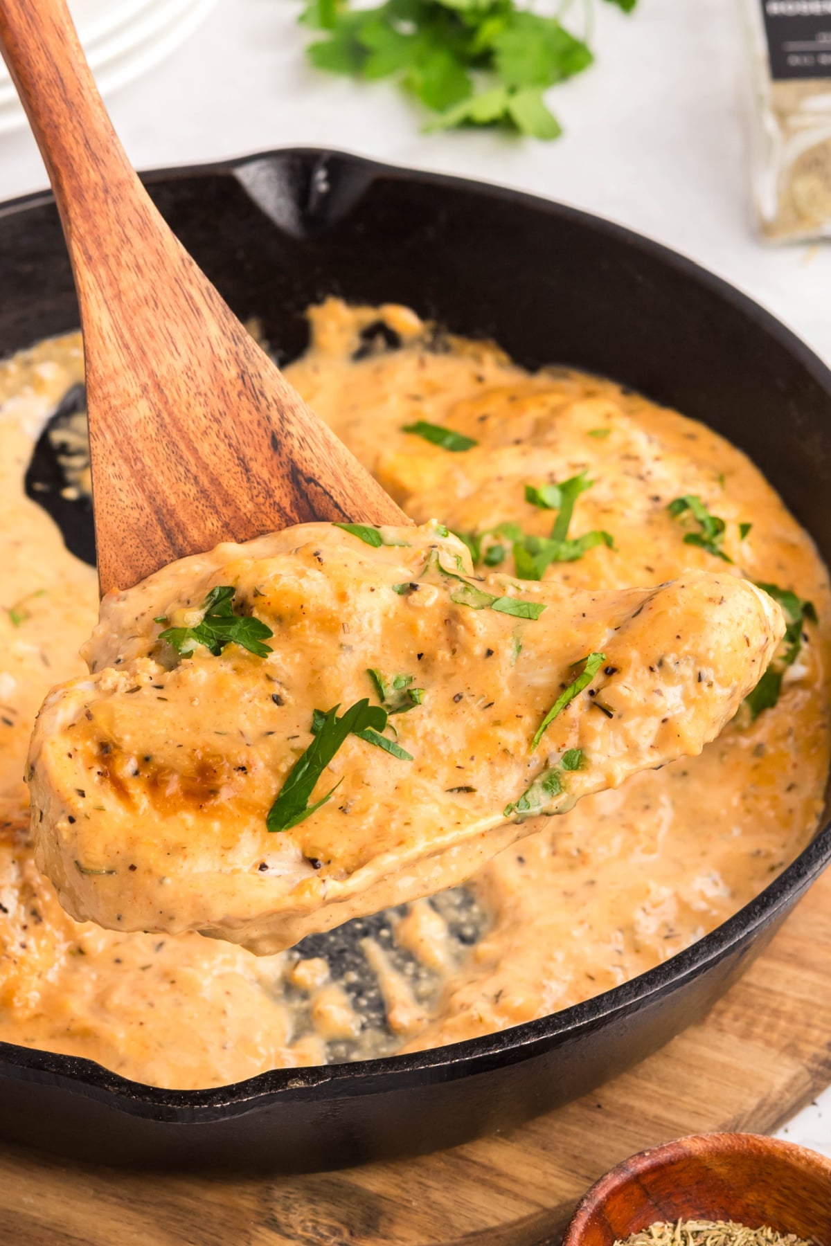 A piece of garlic chicken being scooped out of the saucepan with a wooden spoon.