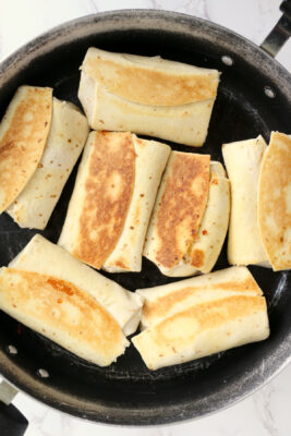 Chicken salad wraps flipped over in the pan with golden brown side up.