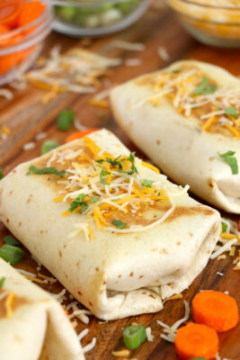 Chicken salad wraps on a cutting board sprinkled with cheese.