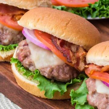 Pork and Bacon Burgers in a bun with toppings on a cutting board