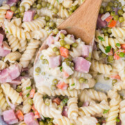 Creamy ham pasta being picked up with a wooden spoon.