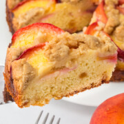 A slice of peach coffee cake held in the air above the cake.