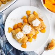 A plate of three peach cobbler dumplings on a plate with whipped cream.
