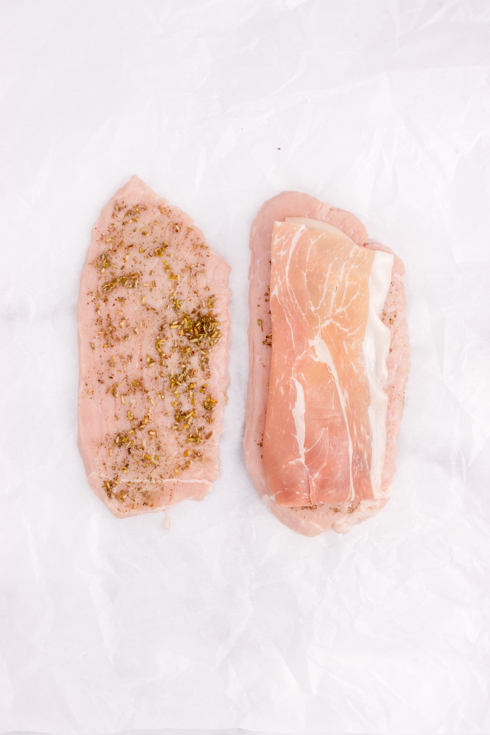 Two slices of veal with herbs on one half and prosciutto.