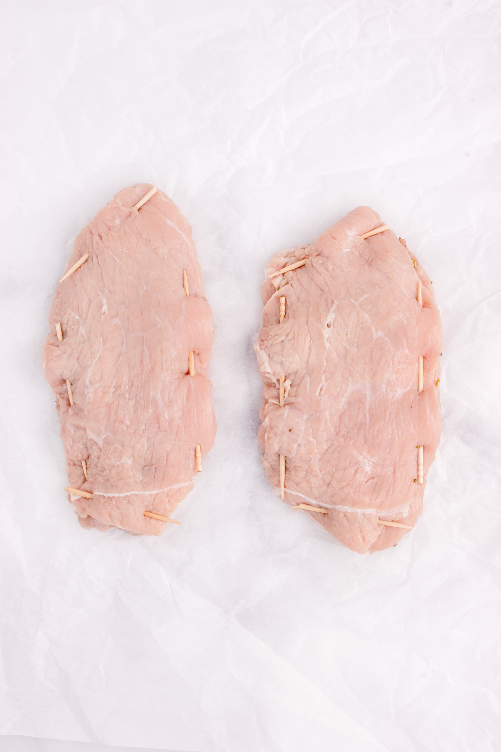 Tow pieces of veal with toothpicks around the edges to keep it sealed.