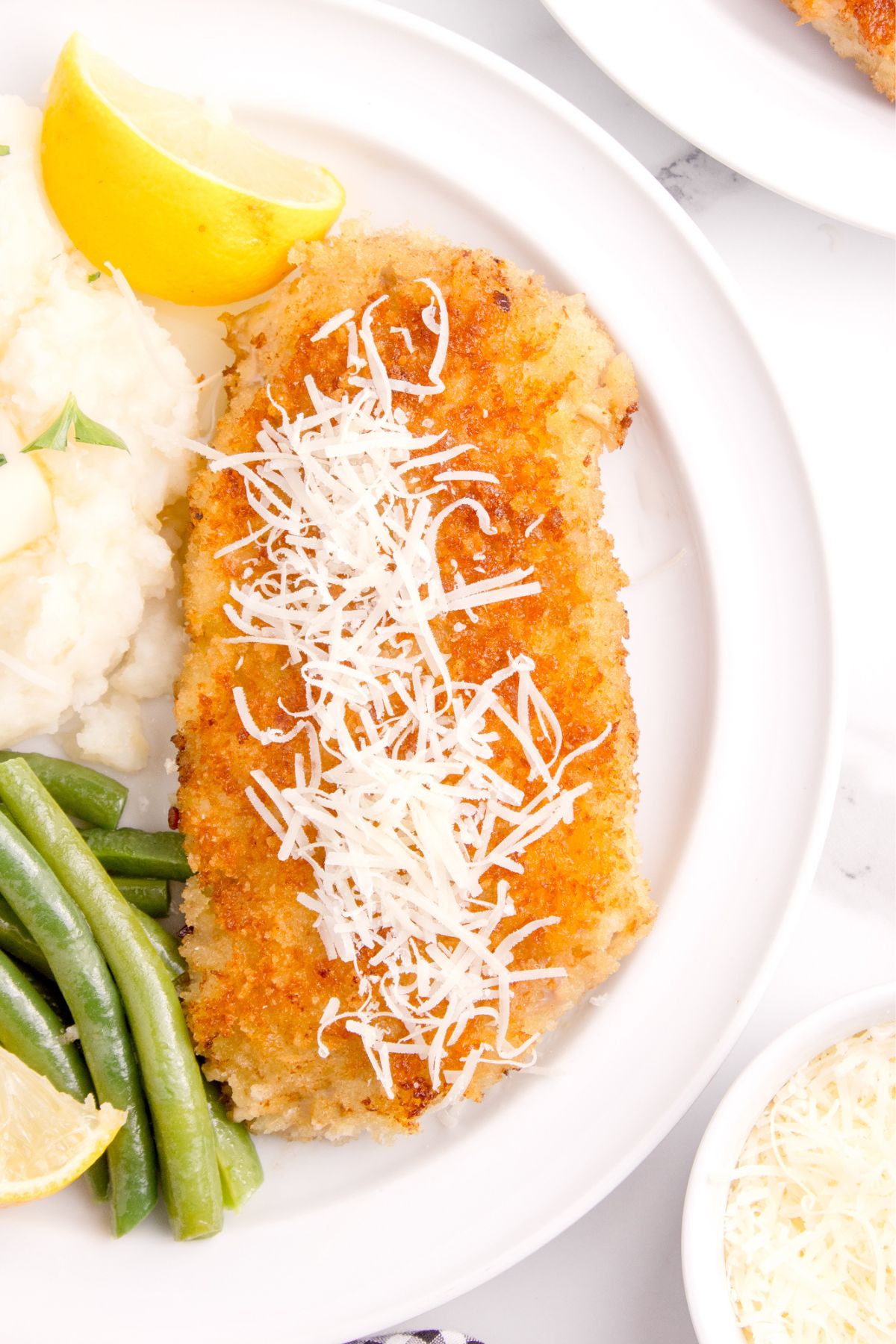 Veal cutlets topped with cheese on top with a side of mashed potatoes and green beans.