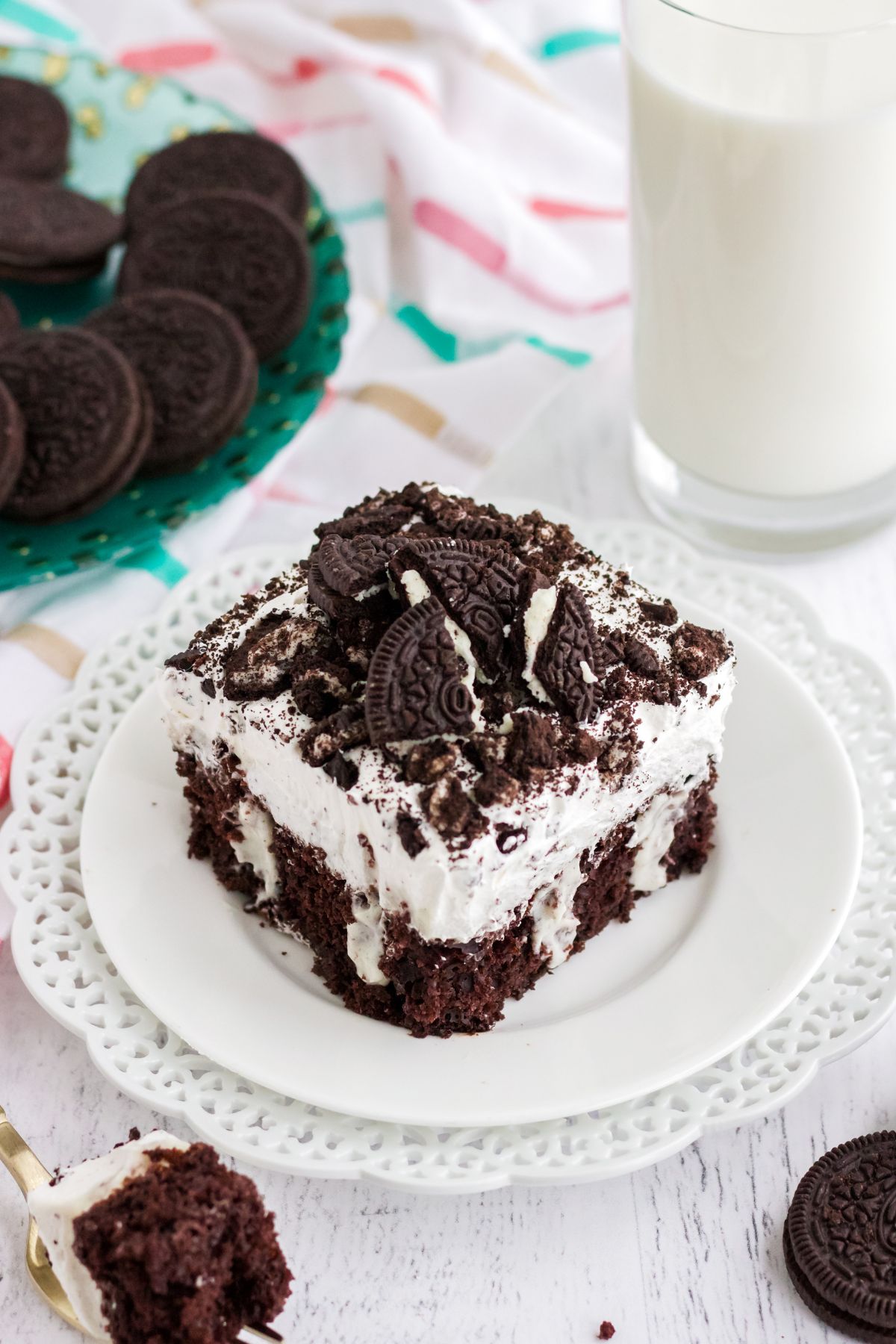 A slice of poke cake with cookies crumbled on top on a white plate