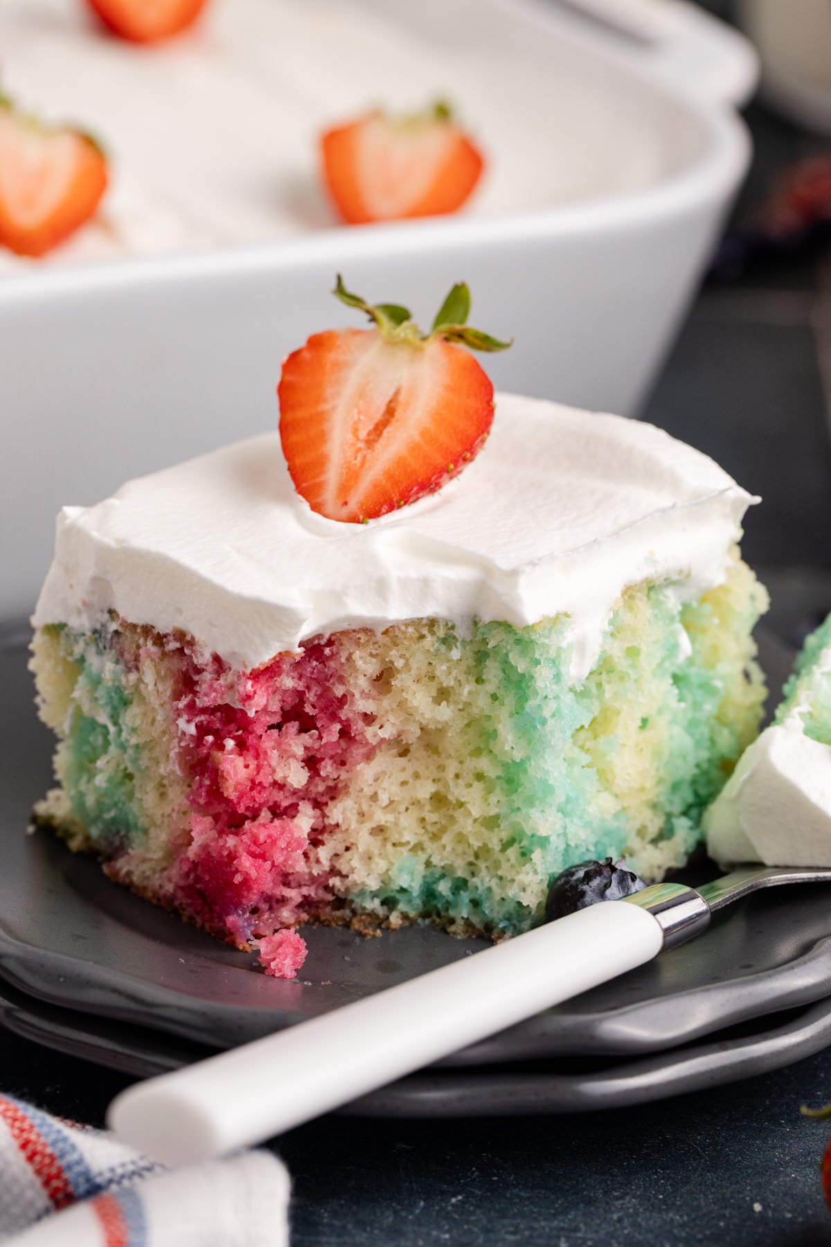 Poke cake with Jello topped with a strawberry and a fork bite taken out.