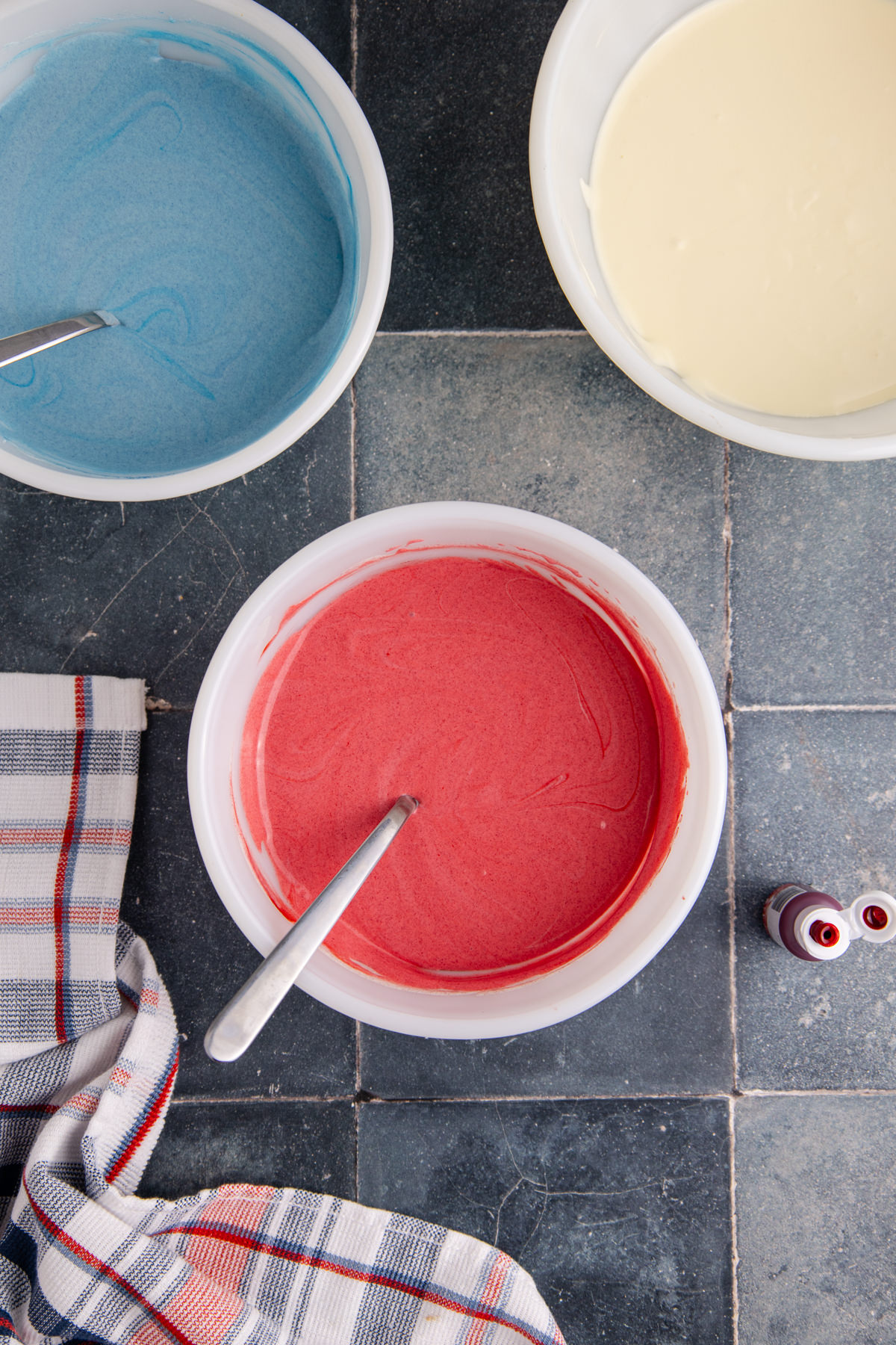 Red cheesecake batter in a bowl with bowls of blue and white to the side.