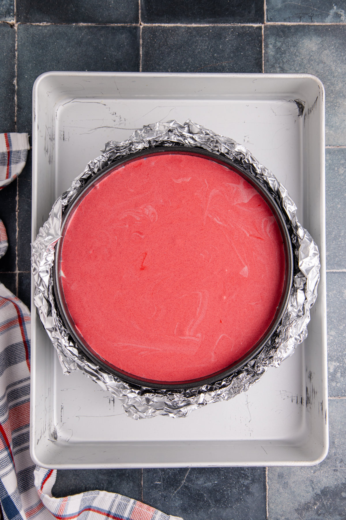 Red cheesecake batter over top of the white and blue batter in a springform pan.