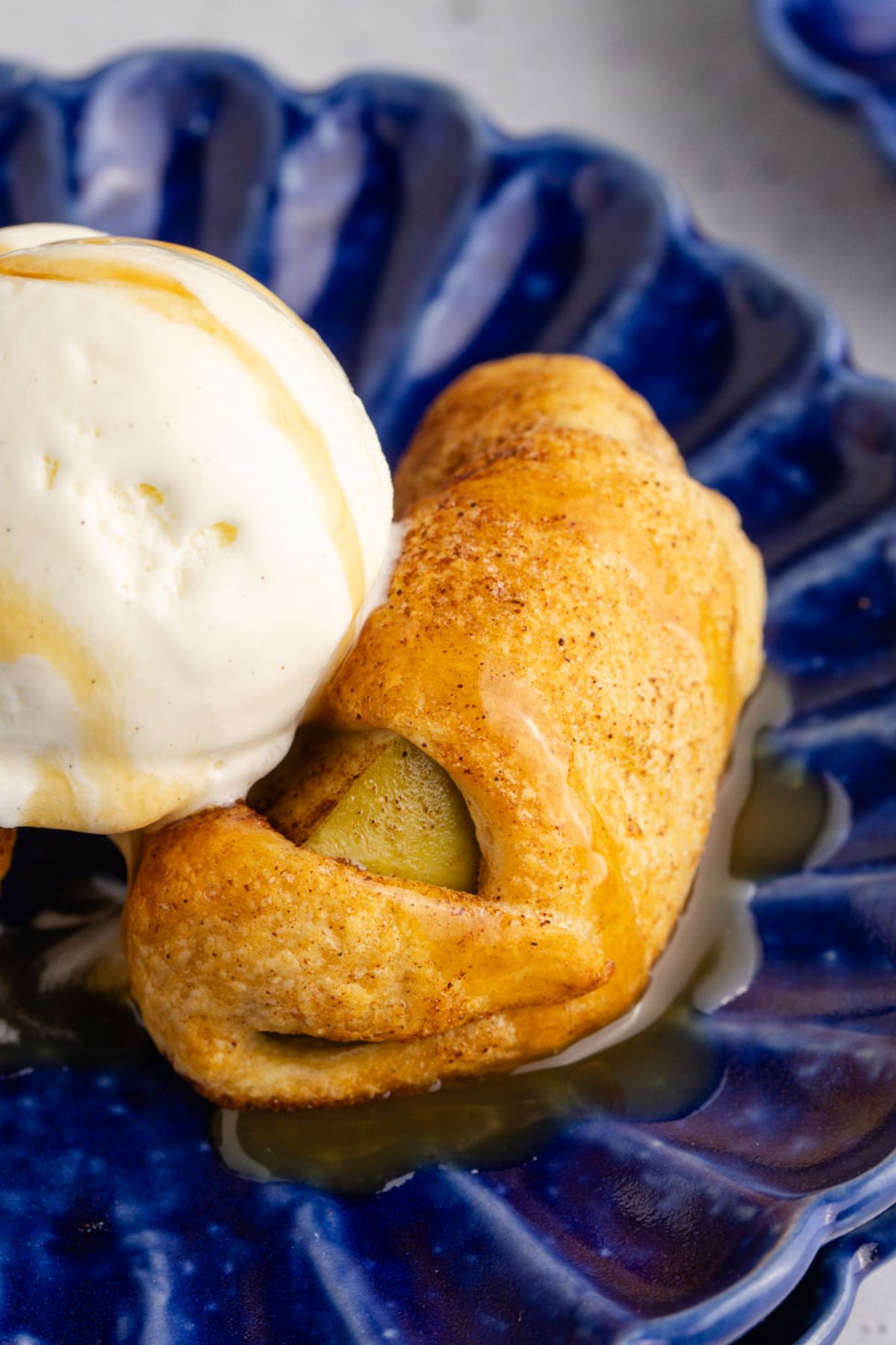 One apple dumpling on a blue plate with a scoop of ice cream.