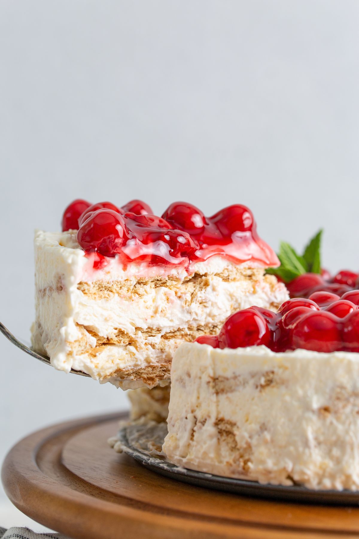 A slice of cheesecake with cherry filling on top being raised with a spatula.