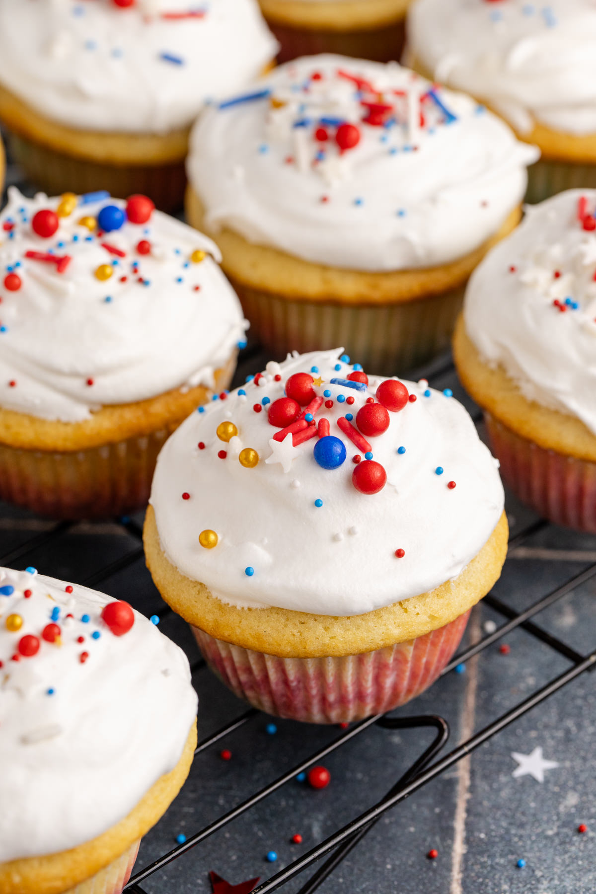 A rack full of cupcakes with sprinkles and cool whip topping.