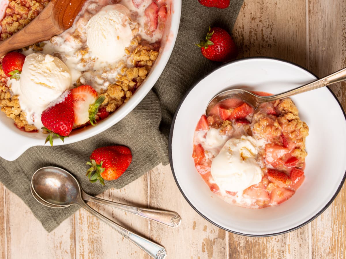 2 bowls of Strawberry Crisp with spoons beside bowls and strawberries