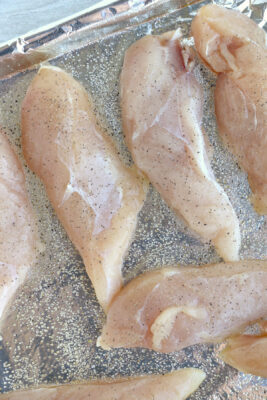 Chicken tenders placed on a greased baking sheet lined with aluminum foil. The chicken tenders are seasoned with salt and pepper.