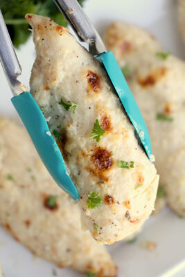 Closeup photo of a pair of tongs holding a cooked chicken tender.