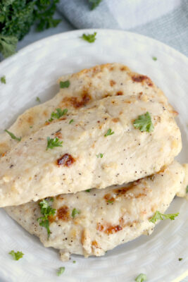 Closeup photo of cooked chicken tenders served on a white plate and garnished with herbs.