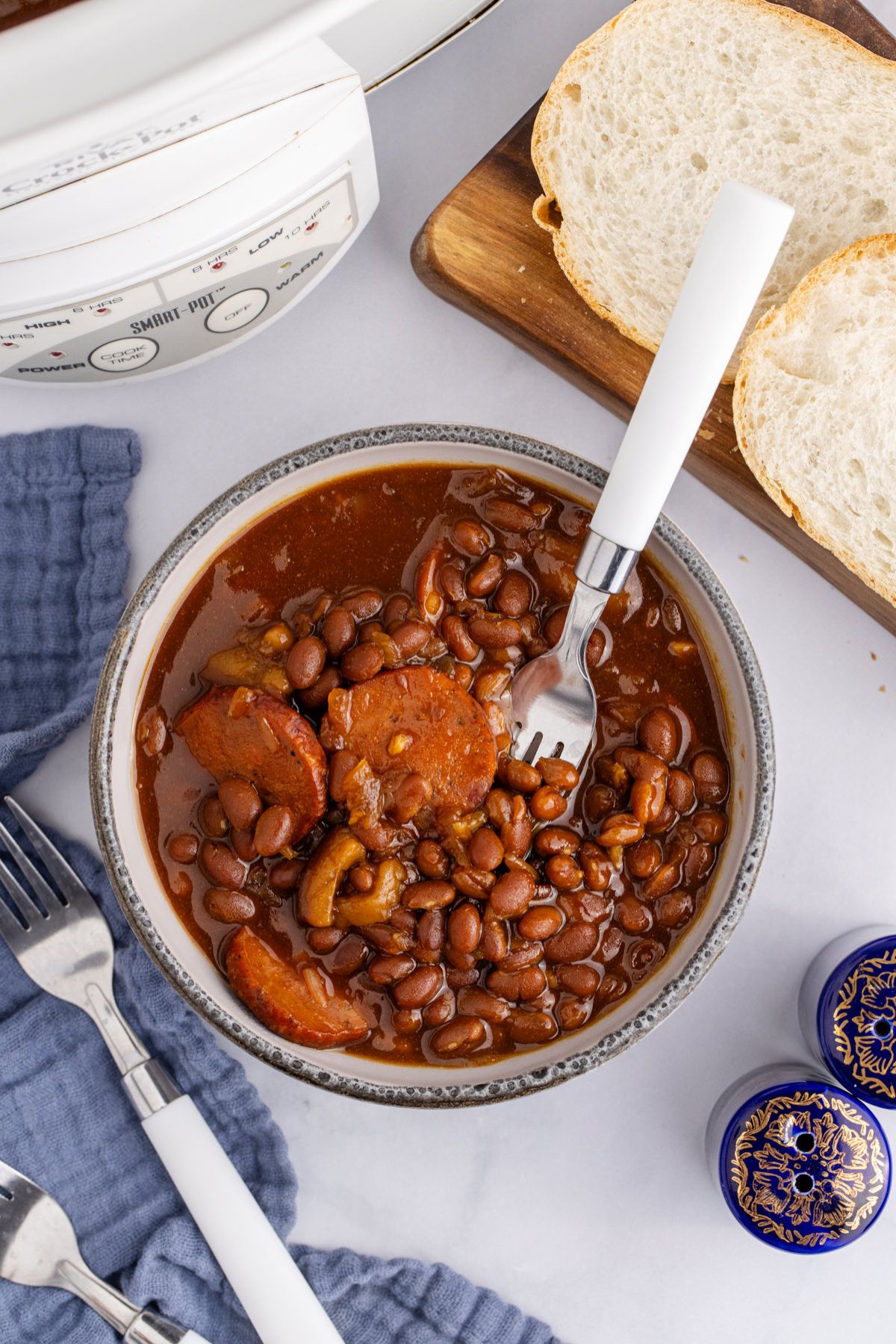 A bowl of slow cooker baked beans with sausage with a fork resting in the dish.