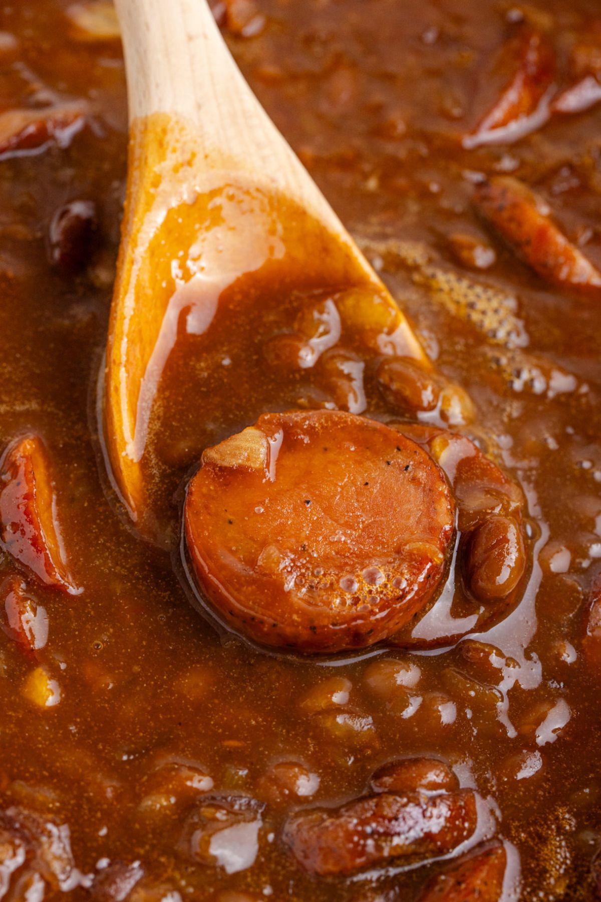 A wooden spoon picking up beans and kielbasa.