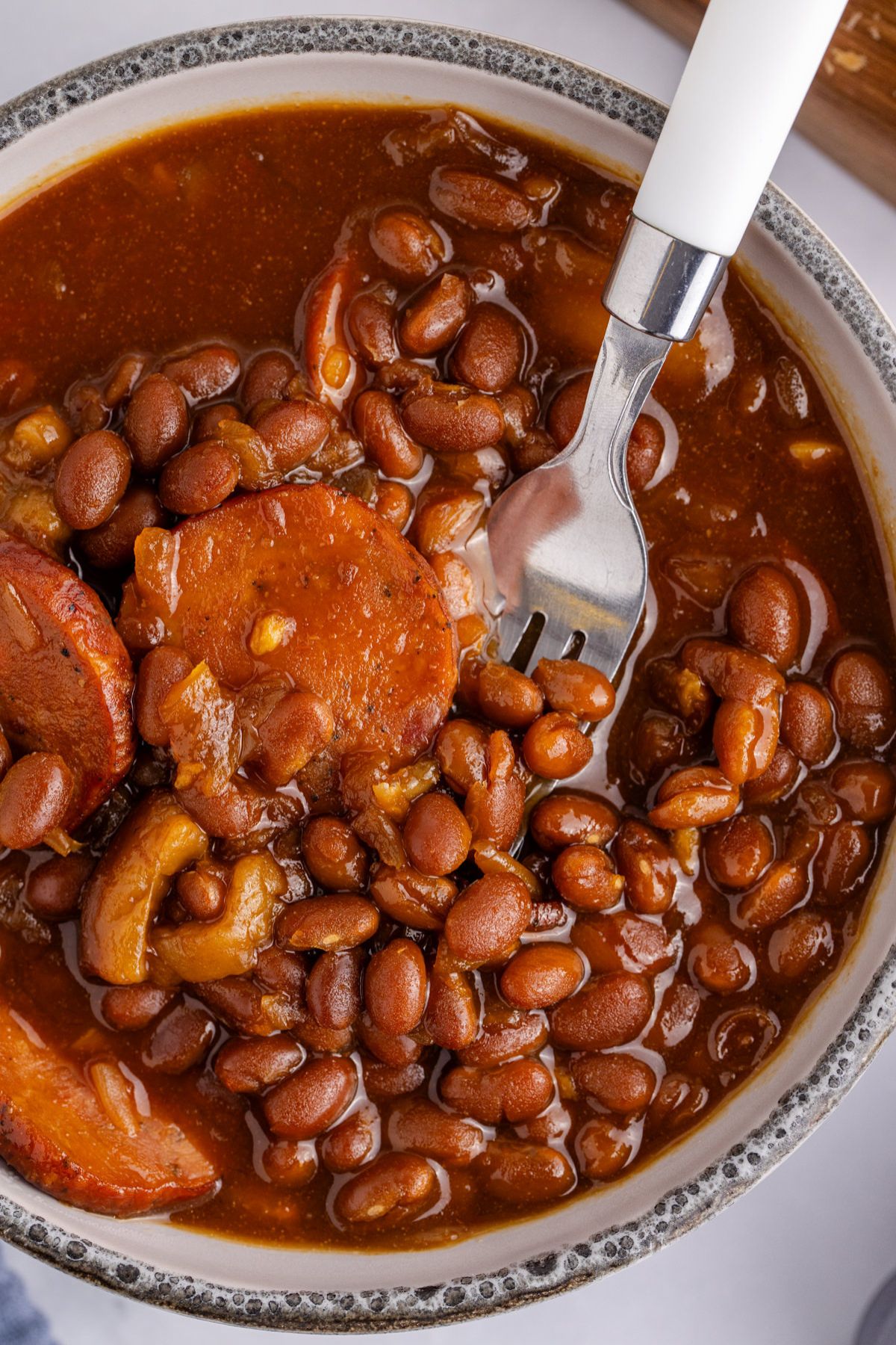 A bowl with kielbasa and beans and a fork to serve.