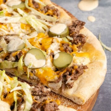 Big mac pizza sliced on a wooden cutting board.