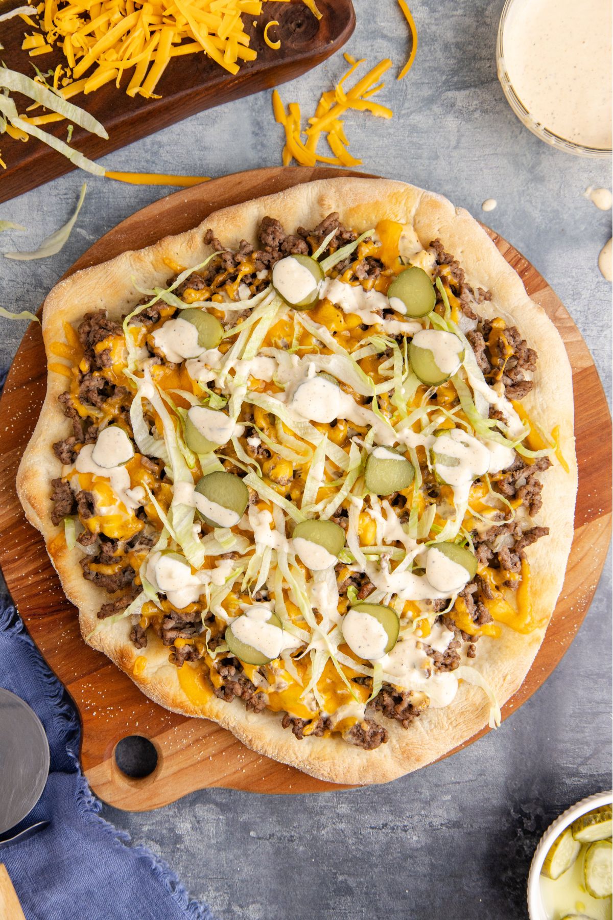 The pizza topped with lettuce, pickle slices, and a drizzle of sauce.